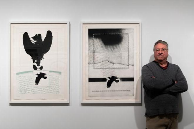 curator Joseph Scheer posing next to two prints on display