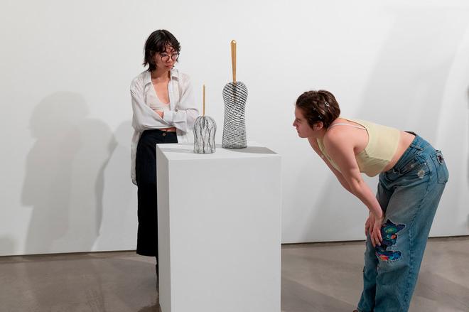 people looking closely at two small glass sculptures on display